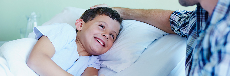 快乐的男孩握着父亲的手躺在病床床上的床上