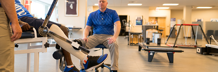 一名运动康复病人在两名理疗师的注视下用他的腿举重。