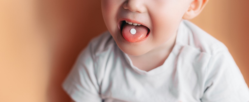 一个孩子伸出舌头，嘴里含着药丸。