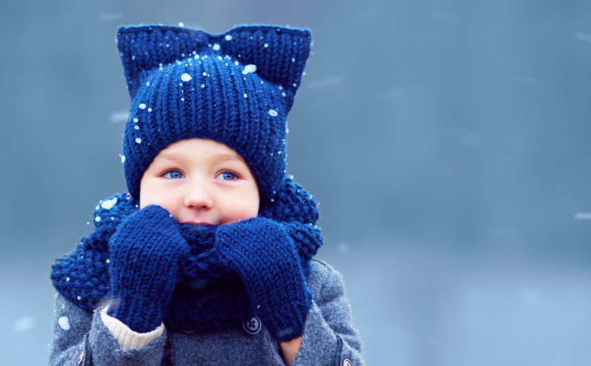 一个戴着连指手套和针织帽的孩子在外面的雪地里。