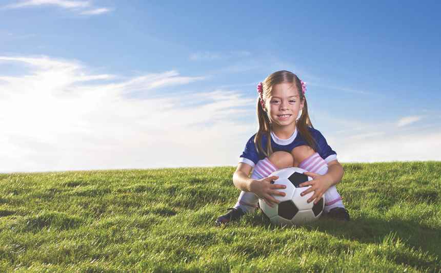 一个小女孩抱着足球坐在草地上。
