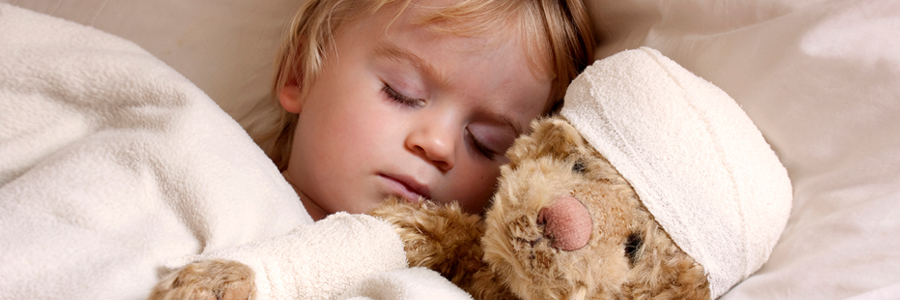 一个小男孩睡在医院的病床上，他的泰迪熊身上缠着绷带。