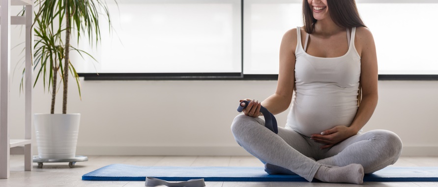 一位孕妇盘腿坐在瑜伽垫上准备伸展。