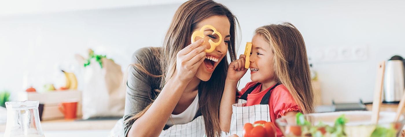 一位母亲和她的女儿一起笑看看甜椒戒指,而切蔬菜沙拉。