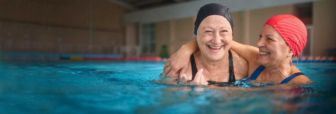 两个戴着泳帽和泳衣的老妇人在游泳池里笑着。