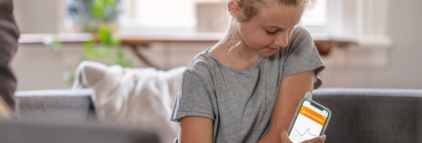 一个十岁前的女孩用她的智能手机检查她的连续血糖监测仪传输的高血糖读数。