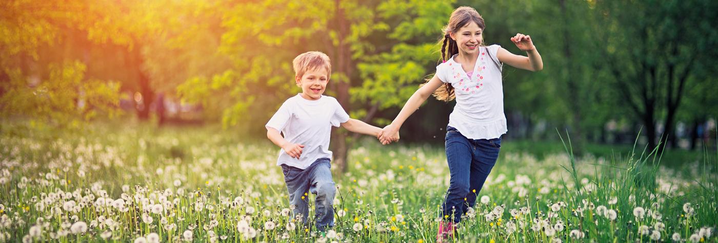 一个小男孩和一个小女孩手牵着手一起跑过一片野花。