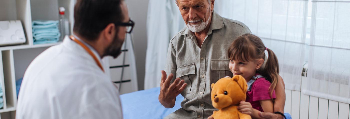 医生和一个抱着泰迪熊的小女孩说话，她的家人也陪着她去看医生。