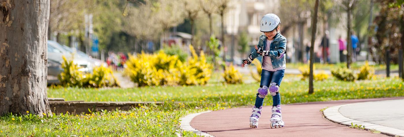一个小女孩在公园里戴着膝盖，肘部垫和头盔旱冰鞋。