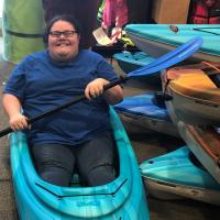 照片在运动器材商店显示艾比微笑着坐在皮艇而假装行她持有的桨。