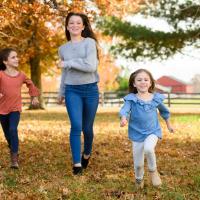 坦诚的照片三个肖尼西女孩一起跑着穿过秋叶,Kailey领先。