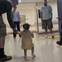 坦诚的照片马克斯牵着年轻Kailey的手,因为他们走在医院的走廊里,几个人看着。